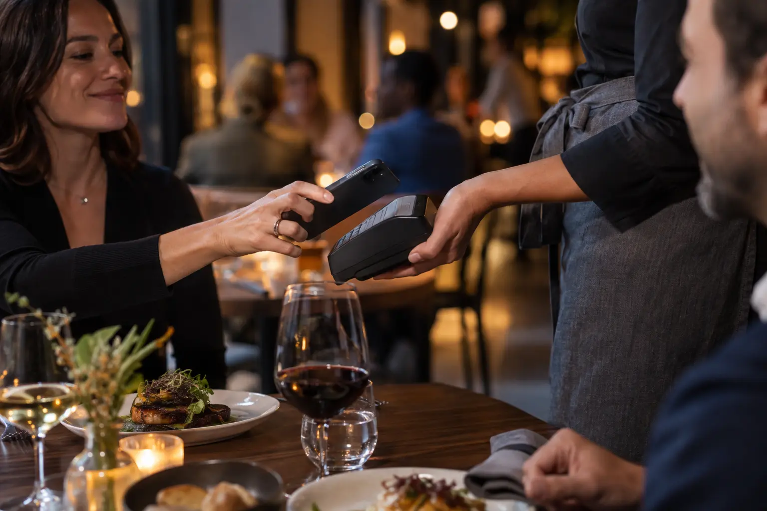 A guest paying at the table by tapping a phone on a handheld